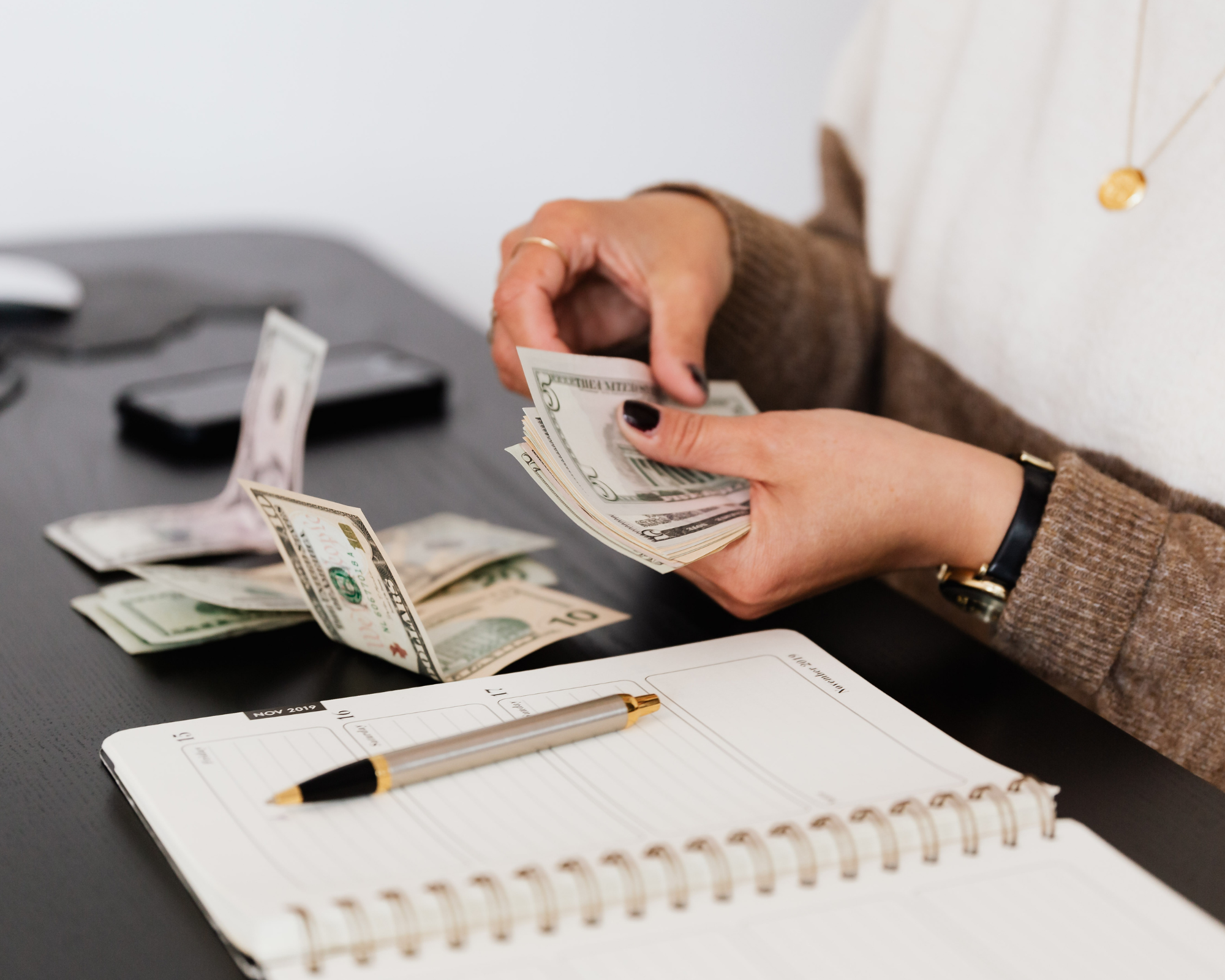 A woman holding money with a pen and paper in front of her on the desk